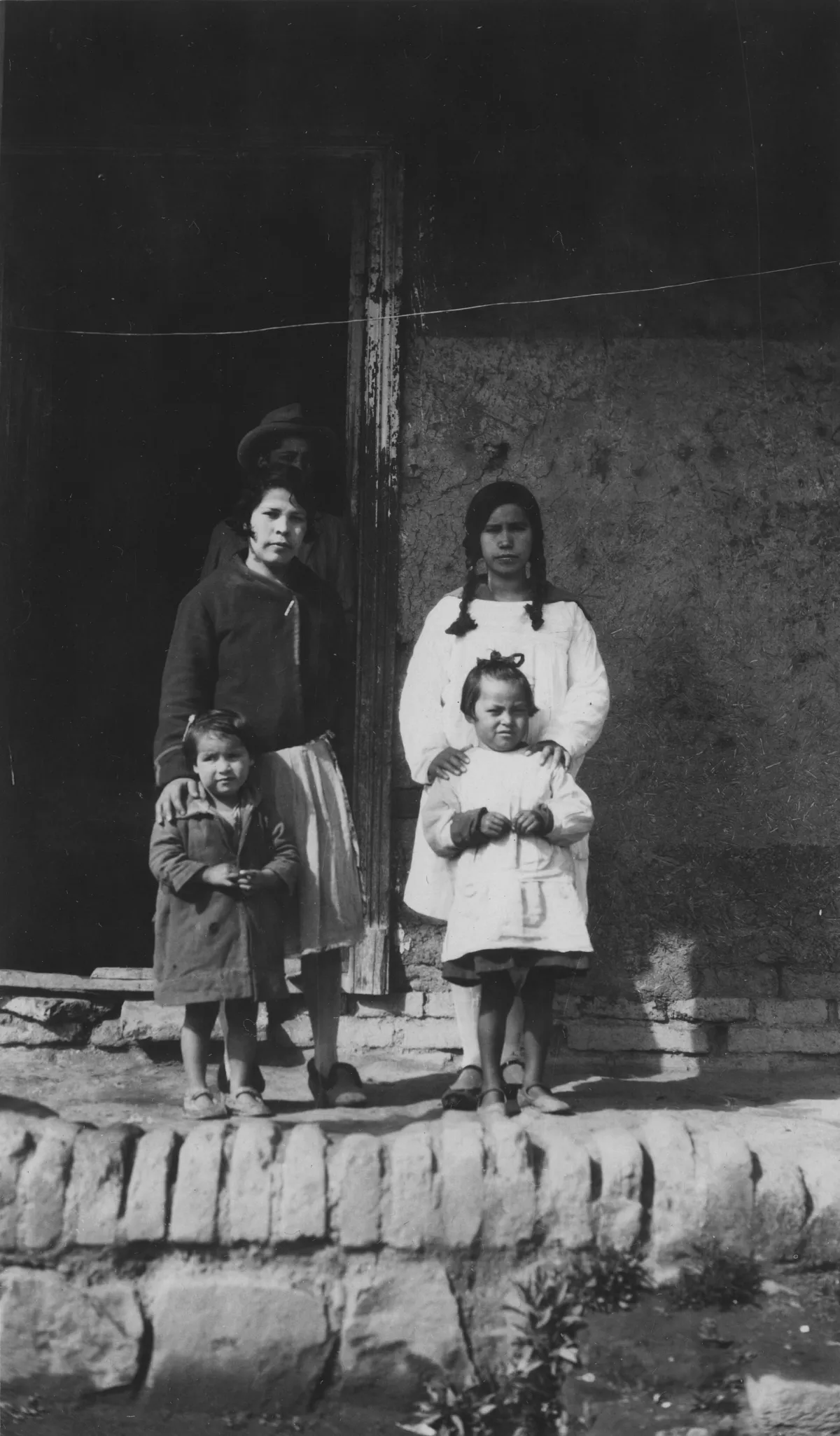 Familia ante muro de adobe con poste de madera — Década de 1940 | Chile de Ayer
