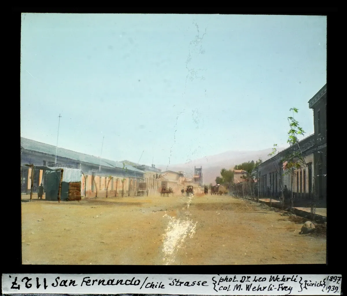 Calle principal de San Fernando con carretas y cordillera al fondo, diapositiva coloreada de 1897 — aprox. 1897–1940 | Chile de Ayer