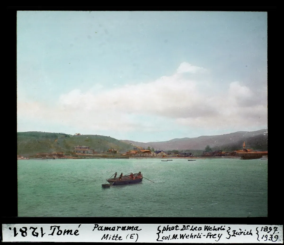 Panorama central de Tome con bote a remo y caserio costero, diapositiva coloreada de 1897 — aprox. 1897–1940 | Chile de Ayer