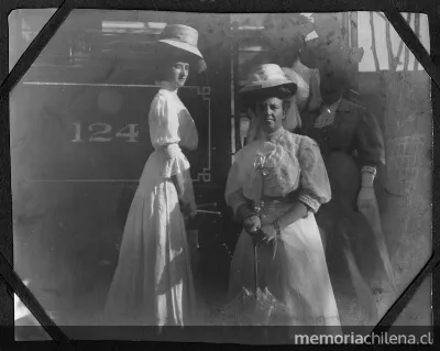 Cuatro señoras, con sombreros, posan en la escalera del tren, portan sombrillas — aprox. 1900 | Chile de Ayer