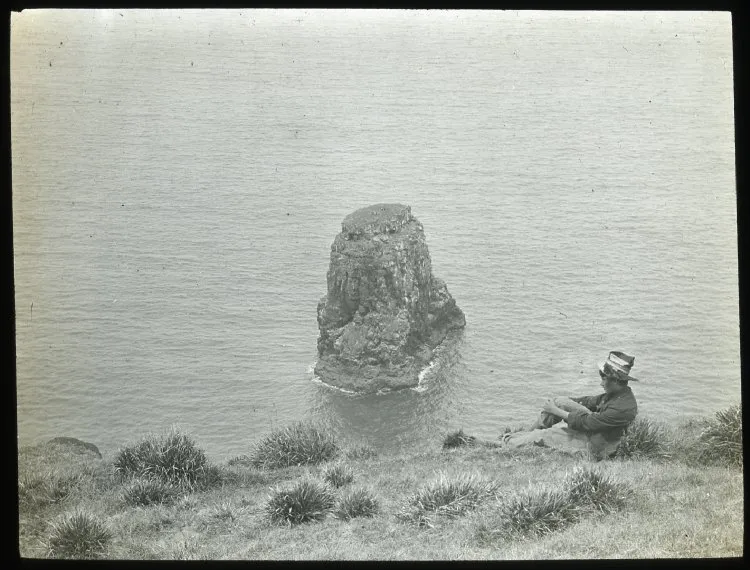 Chilean boy sitting down by cliff with view of Marotiri; Poike, Oc,G.T.1627, Mana Expedition to Easter Island, British Museum — Isla de Pascua — 1914 | Chile de Ayer