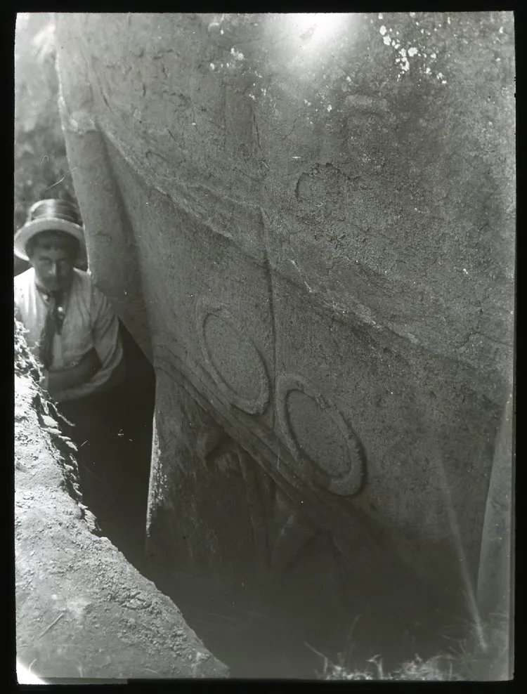 Close up view of the back of a moai excavated but still standing upright in the ground; a man is standing in the excavated gap beside the scultpure for scale; Rano Raraku, Oc,G.T.1476, Mana Expedition to Easter Island, British Museum — Isla de Pascua — 1914 | Chile de Ayer