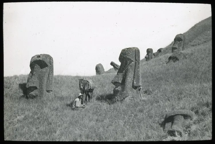 Polynesian(?) man sitting on the ground with a horse next to partially buried moai; Rano Raraku, Oc,G.T.1608, Mana Expedition to Easter Island, British Museum — Isla de Pascua — 1914 | Chile de Ayer