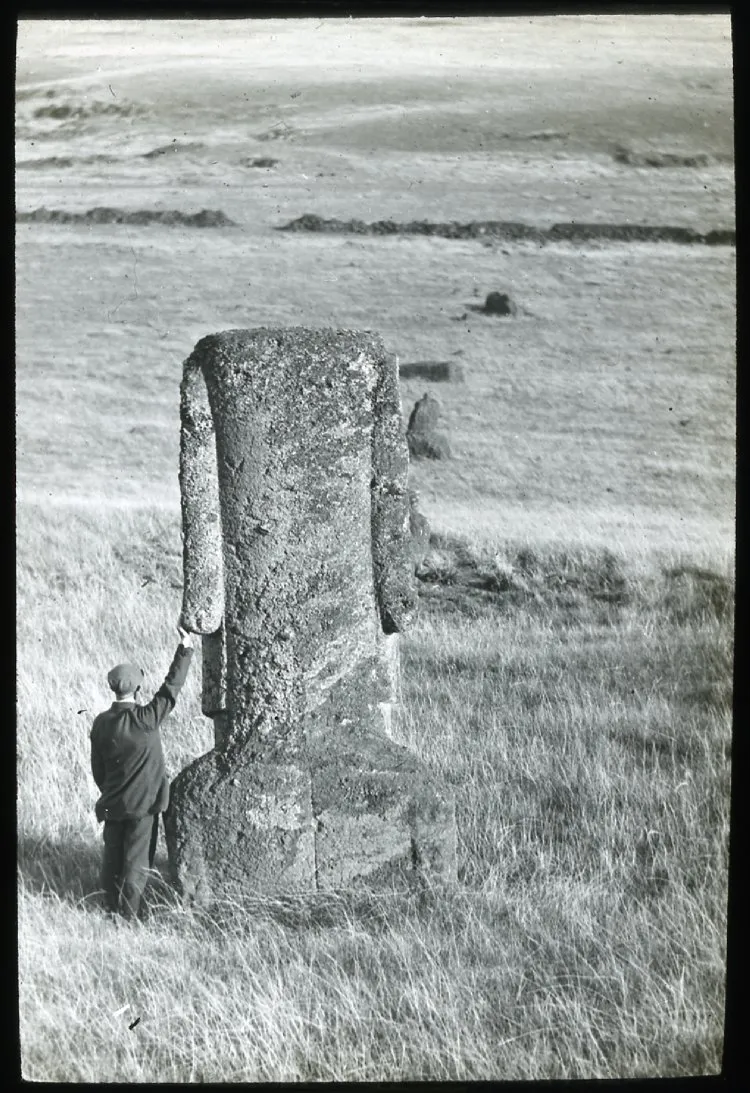 View of a back of moai with a man standing on the left of the sculpture with his back to the camera and one hand on the left earlobe, for scale; Rano Raraku; Oc,G.T.1474, Mana Expedition to Easter Island, British Museum — Isla de Pascua — 1914 | Chile de Ayer