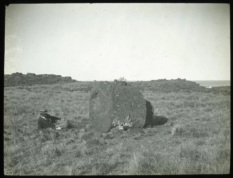 View of a large round stone used as part of a moai, with a White man lying on the ground beside it, for scale; Ahu Hekii, Oc,G.T.1624, Mana Expedition to Easter Island, British Museum — Isla de Pascua — 1914 | Chile de Ayer