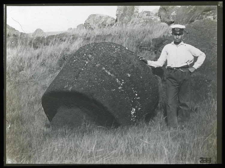 View of a round carved piece of stone, part of a moai, with a man standing beside the stone for scale, Oc,G.T.1499, Mana Expedition to Easter Island, British Museum — Isla de Pascua — 1914 | Chile de Ayer