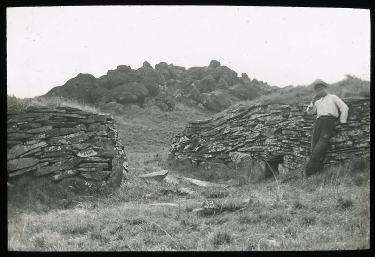 View of stone wall houses, with a Chilean boy standing on the right for scale; Orongo, Oc,G.T.1619, Mana Expedition to Easter Island, British Museum — Isla de Pascua — 1914 | Chile de Ayer