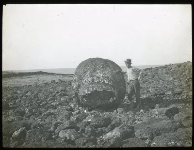 Chilean boy standing beside a large round stone used as part of a moai; Ahu Hekii, Oc,G.T.1623, Mana Expedition to Easter Island, British Museum — Isla de Pascua — 1914 | Chile de Ayer