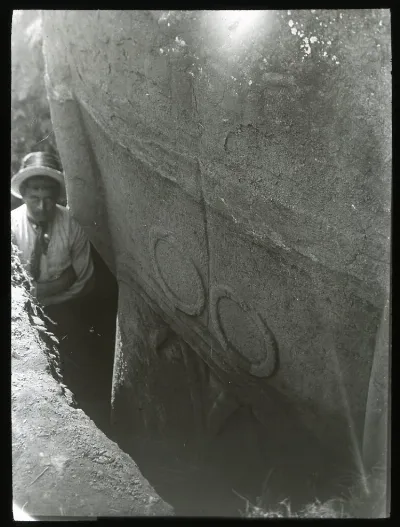 Close up view of the back of a moai excavated but still standing upright in the ground; a man is standing in the excavated gap beside the scultpure for scale; Rano Raraku, Oc,G.T.1476, Mana Expedition to Easter Island, British Museum — Isla de Pascua — 1914 | Chile de Ayer