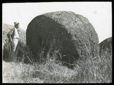 View of a large round stone, to be used as part of a moai, with a Polynesian man standing beside it, for scale; outside of Puna Pau, Oc,G.T.1626, Mana Expedition to Easter Island, British Museum — Isla de Pascua — 1914 | Chile de Ayer