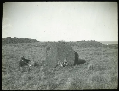 View of a large round stone used as part of a moai, with a White man lying on the ground beside it, for scale; Ahu Hekii, Oc,G.T.1624, Mana Expedition to Easter Island, British Museum — Isla de Pascua — 1914 | Chile de Ayer