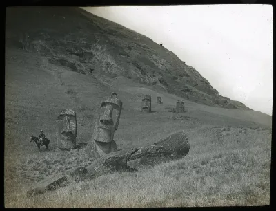 View of a moai lying on the ground, with five moai heads standing upright, buried in the ground; a man is sitting on a horse on the left of the image for scale; Rano Raraku, Oc,G.T.1478, Mana Expedition to Easter Island, British Museum — Isla de Pascua — 1914 | Chile de Ayer