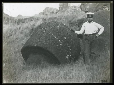 View of a round carved piece of stone, part of a moai, with a man standing beside the stone for scale, Oc,G.T.1499, Mana Expedition to Easter Island, British Museum — Isla de Pascua — 1914 | Chile de Ayer