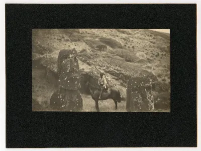 View of hill, with two moai (stone figure carving heads) visible; a boy sitting on a horse in between both sculptures; Rano Raraku, Oc,B30.11, Mana Expedition to Easter Island, British Museum — Isla de Pascua — 1914 | Chile de Ayer