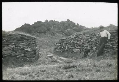 View of stone wall houses, with a Chilean boy standing on the right for scale; Orongo, Oc,G.T.1619, Mana Expedition to Easter Island, British Museum — Isla de Pascua — 1914 | Chile de Ayer