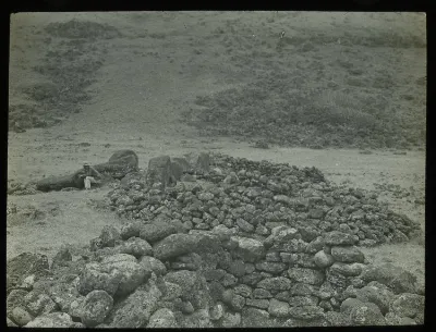 View of two manavai areas, and a fallen moai, with a Polynesian man wearing a plant fibre hat, sitting down for scale; Ahu Te Pa Haha Tea, Oc,G.T.1621, Mana Expedition to Easter Island, British Museum — Isla de Pascua — 1914 | Chile de Ayer