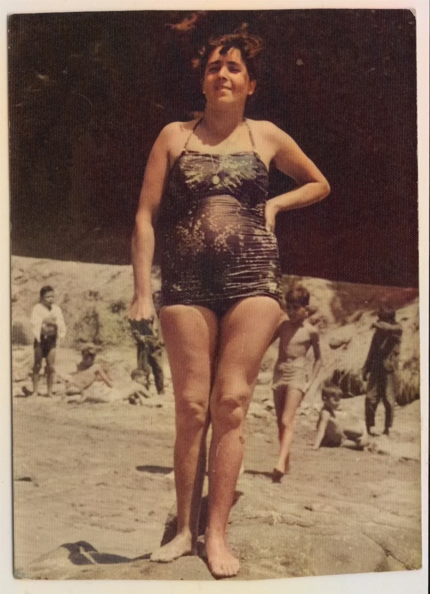 Mujer posando en traje de baño plisado, playa con bañistas al fondo — 1955 | Chile de Ayer