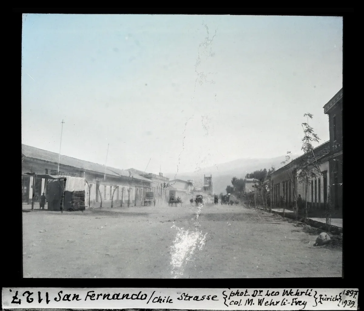 Calle principal de San Fernando con carretas y cordillera al fondo, diapositiva coloreada de 1897 — aprox. 1897–1940 | Chile de Ayer