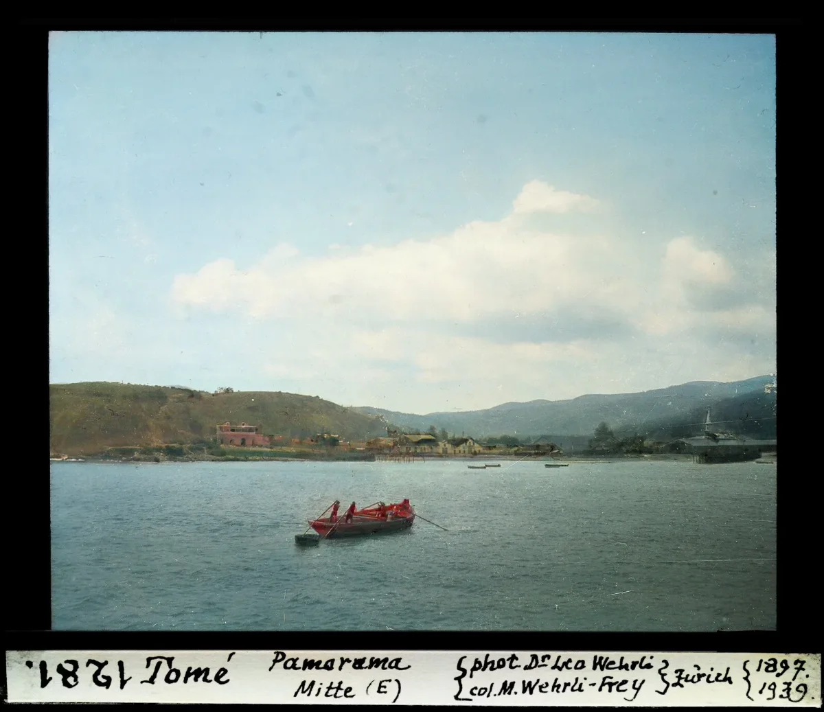 Panorama central de Tome con bote a remo y caserio costero, diapositiva coloreada de 1897 — aprox. 1897–1940 | Chile de Ayer