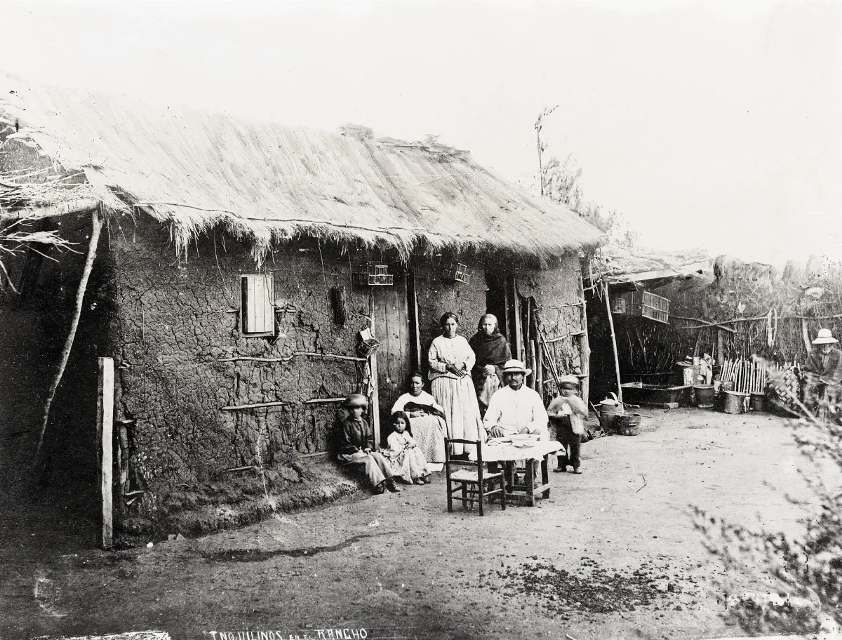 Inquilinos frente a casa de adobe con techo de paja — aprox. 1900–1930 | Chile de Ayer