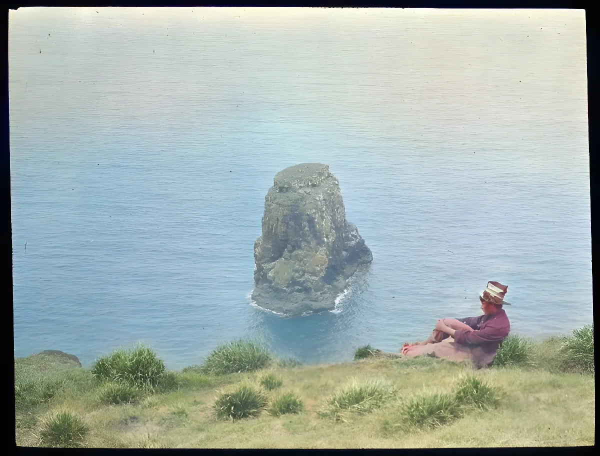 Chilean boy sitting down by cliff with view of Marotiri; Poike, Oc,G.T.1627, Mana Expedition to Easter Island, British Museum — Isla de Pascua — 1914 | Chile de Ayer