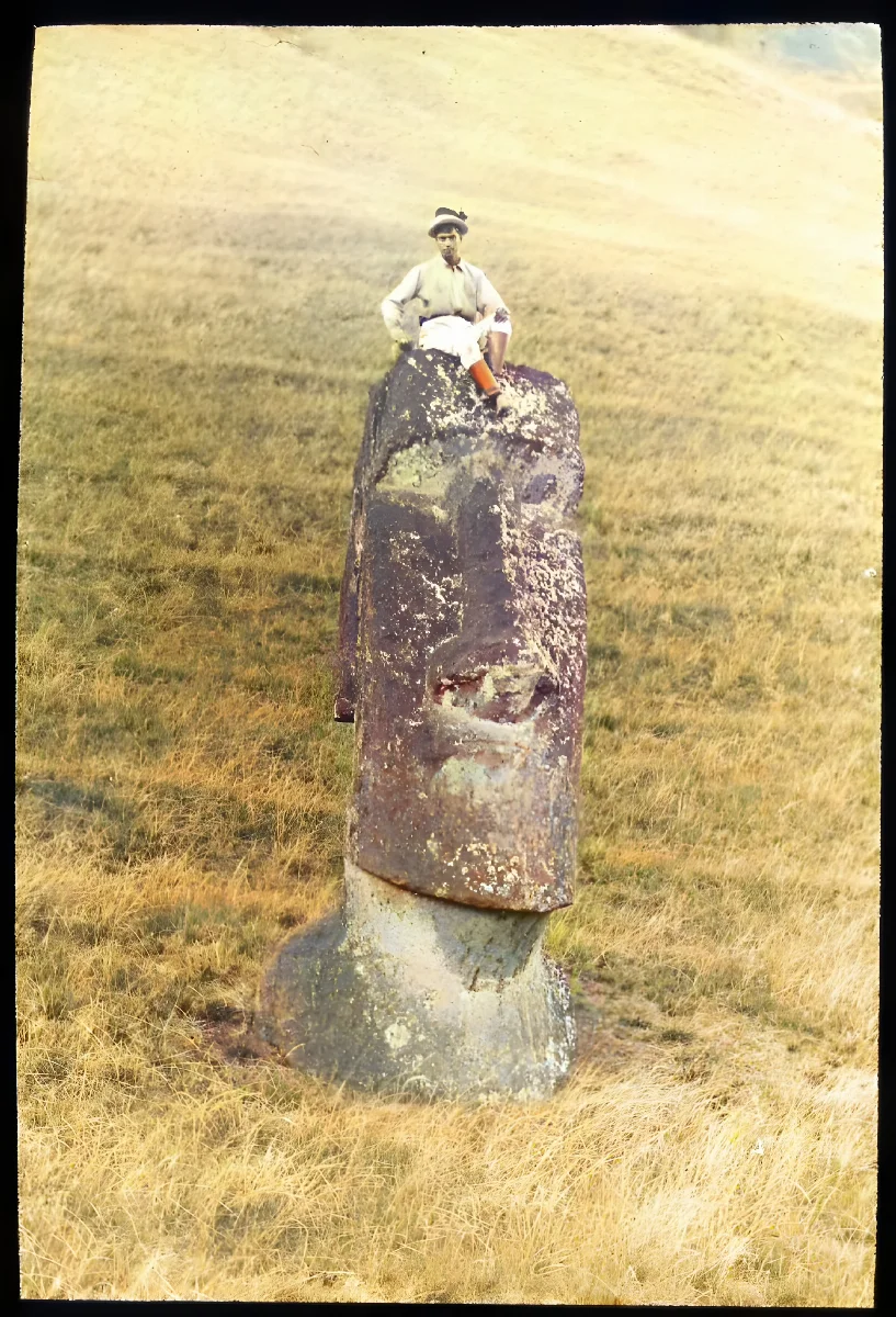 View of a moai head standing upright in the ground, with a boy sitting on top of the carved head for scale; Rano Raraku, Oc,G.T.1467, Mana Expedition to Easter Island, British Museum — Isla de Pascua — 1914 | Chile de Ayer