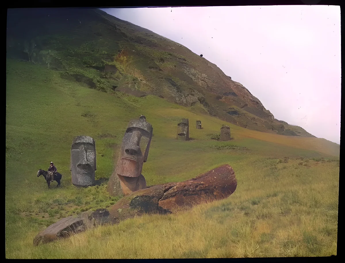 View of a moai lying on the ground, with five moai heads standing upright, buried in the ground; a man is sitting on a horse on the left of the image for scale; Rano Raraku, Oc,G.T.1478, Mana Expedition to Easter Island, British Museum — Isla de Pascua — 1914 | Chile de Ayer