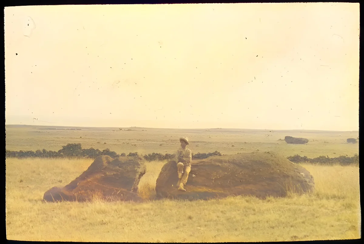 View of a moai lying on the ground; a man is standing on the left of the sculpture for scale, with his left hand touching the stone; outside Rano Raraku, Oc,G.T.1464, Mana Expedition to Easter Island, British Museum — Isla de Pascua — 1914 | Chile de Ayer