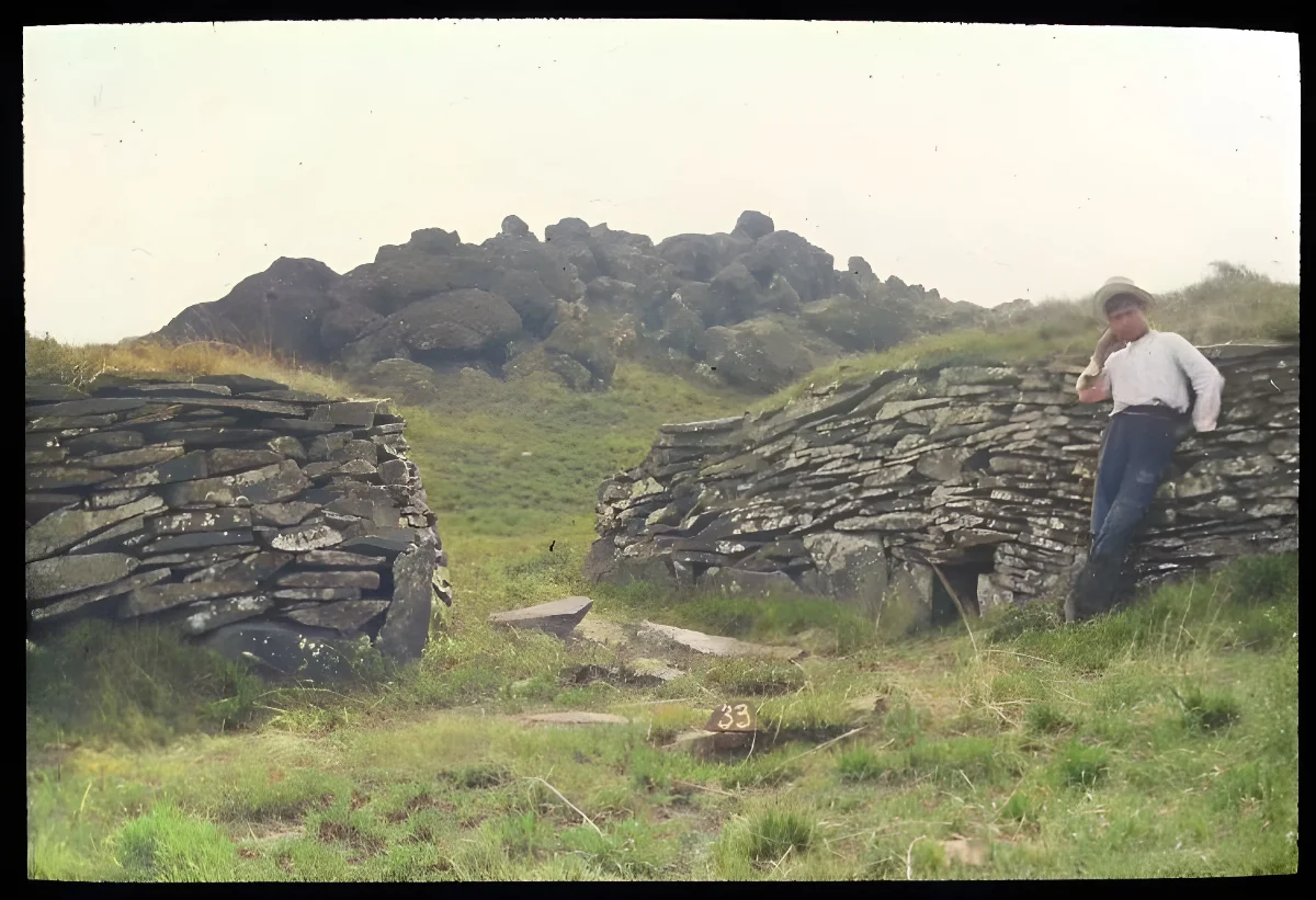 View of stone wall houses, with a Chilean boy standing on the right for scale; Orongo, Oc,G.T.1619, Mana Expedition to Easter Island, British Museum — Isla de Pascua — 1914 | Chile de Ayer