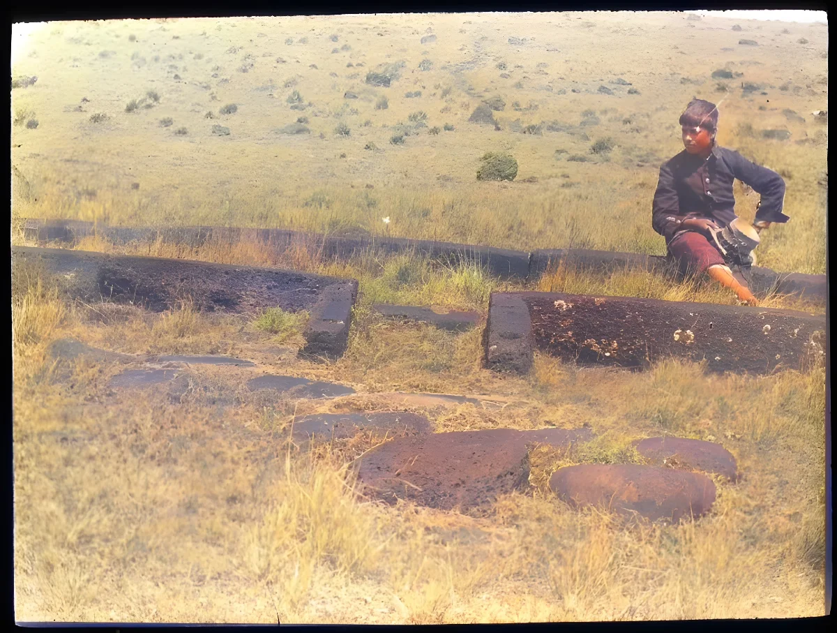 View of the foundation for the door and front of a hare paenga, with a Chilean(?) boy sitting on one of the stones, for scale; Easter Island, Oc,G.T.1638, Mana Expedition to Easter Island, British Museum — Isla de Pascua — 1914 | Chile de Ayer