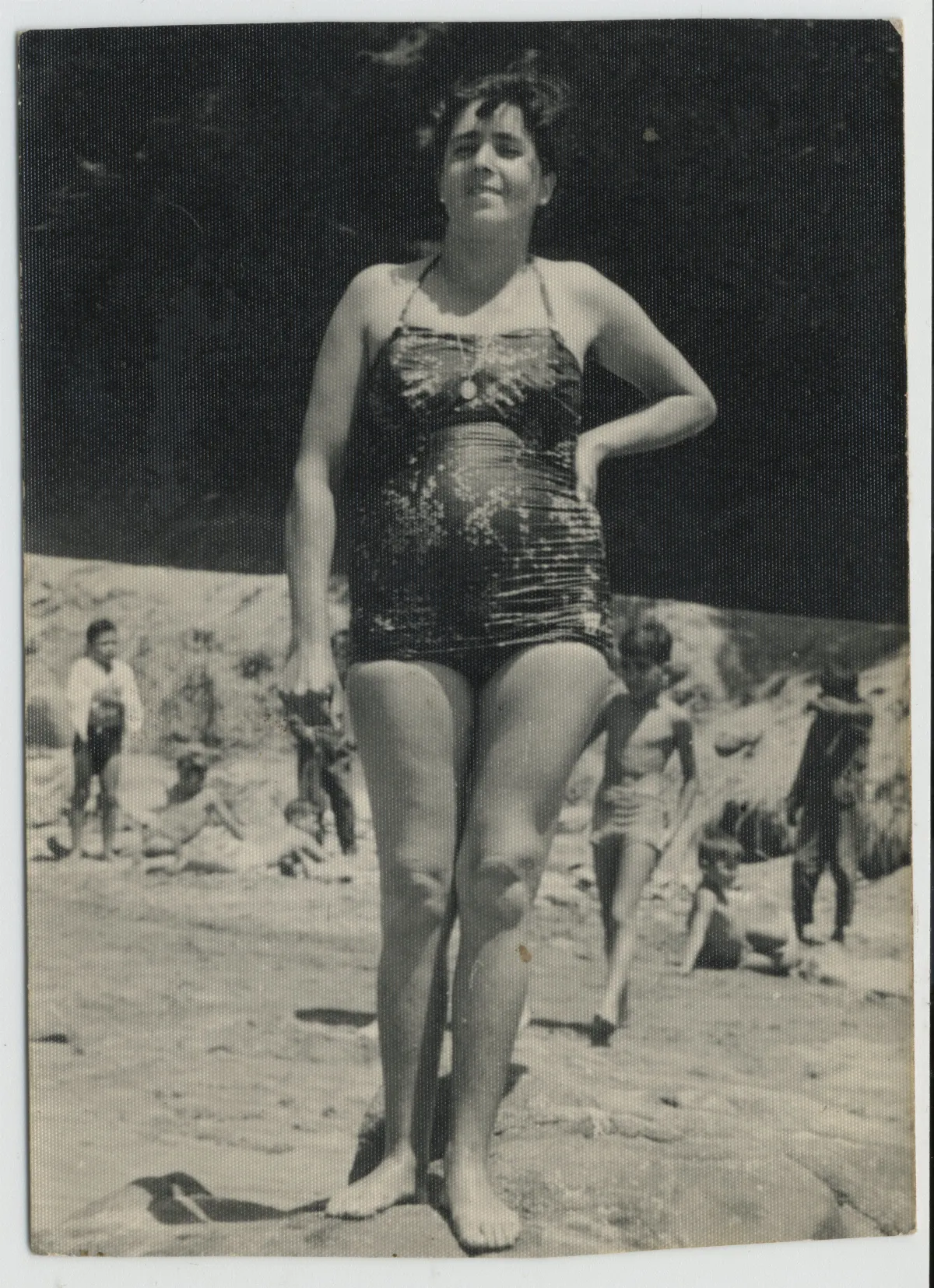 Mujer posando en traje de baño plisado, playa con bañistas al fondo — 1955 | Chile de Ayer