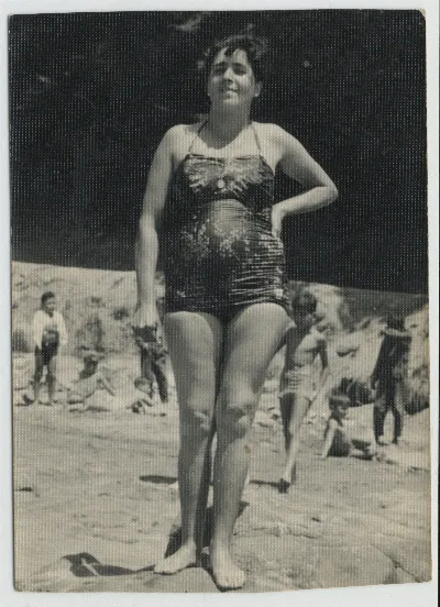 Mujer posando en traje de baño plisado, playa con bañistas al fondo — 1955 | Chile de Ayer